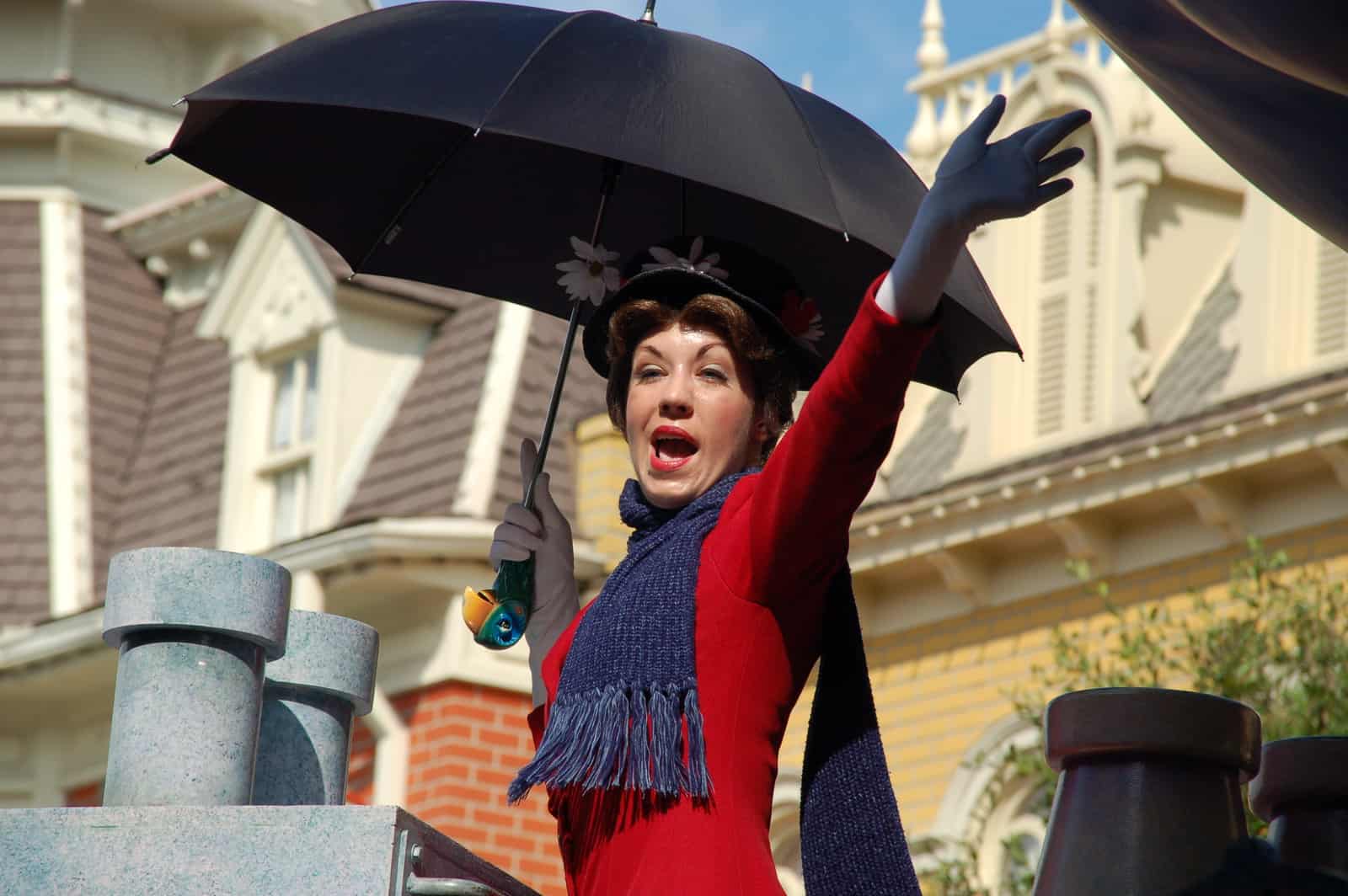Image of Mary Poppins in red dress with purple scarf carrying black umbrella
